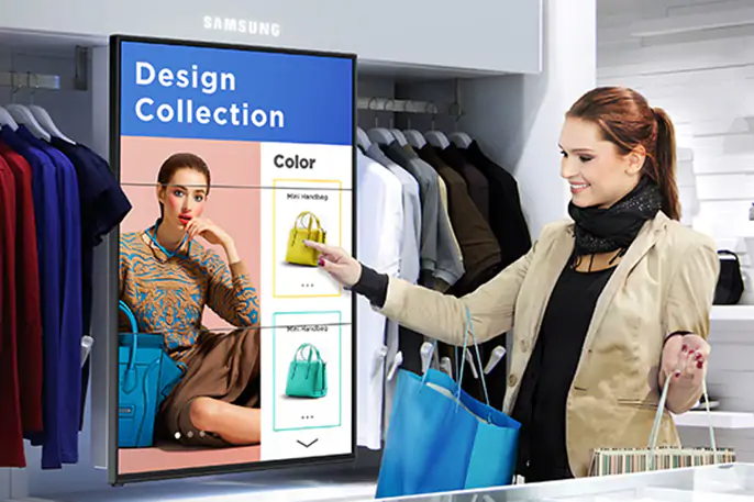 Una mujer en una tienda de ropa, con bolsas en los brazos mientras interactua con una pantalla táctil que muestra variaciones de ropa